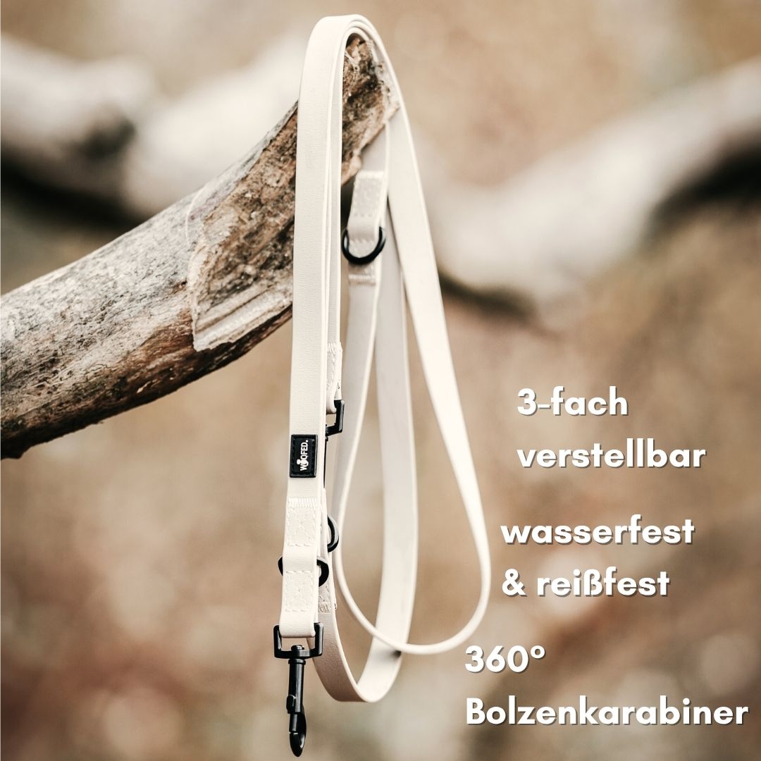Sandfarbene WOOFLEX‑Leine, 3‑fach verstellbar, hängend an Ast mit schwarzem Bolzenkarabiner und Ringen