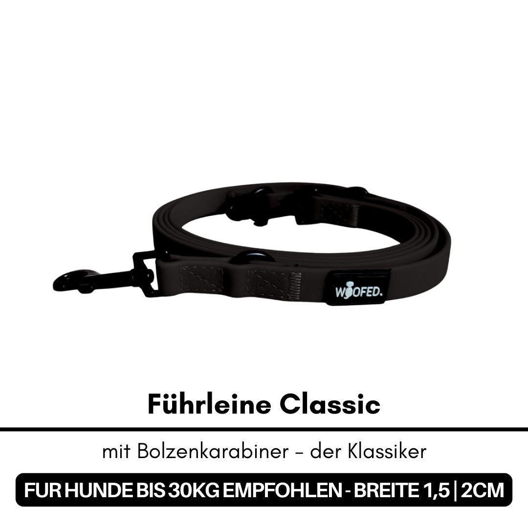 Aufgerollte schwarze Führleine mit Bolzenkarabiner und WOOFED-Label, liegend auf weißem Hintergrund