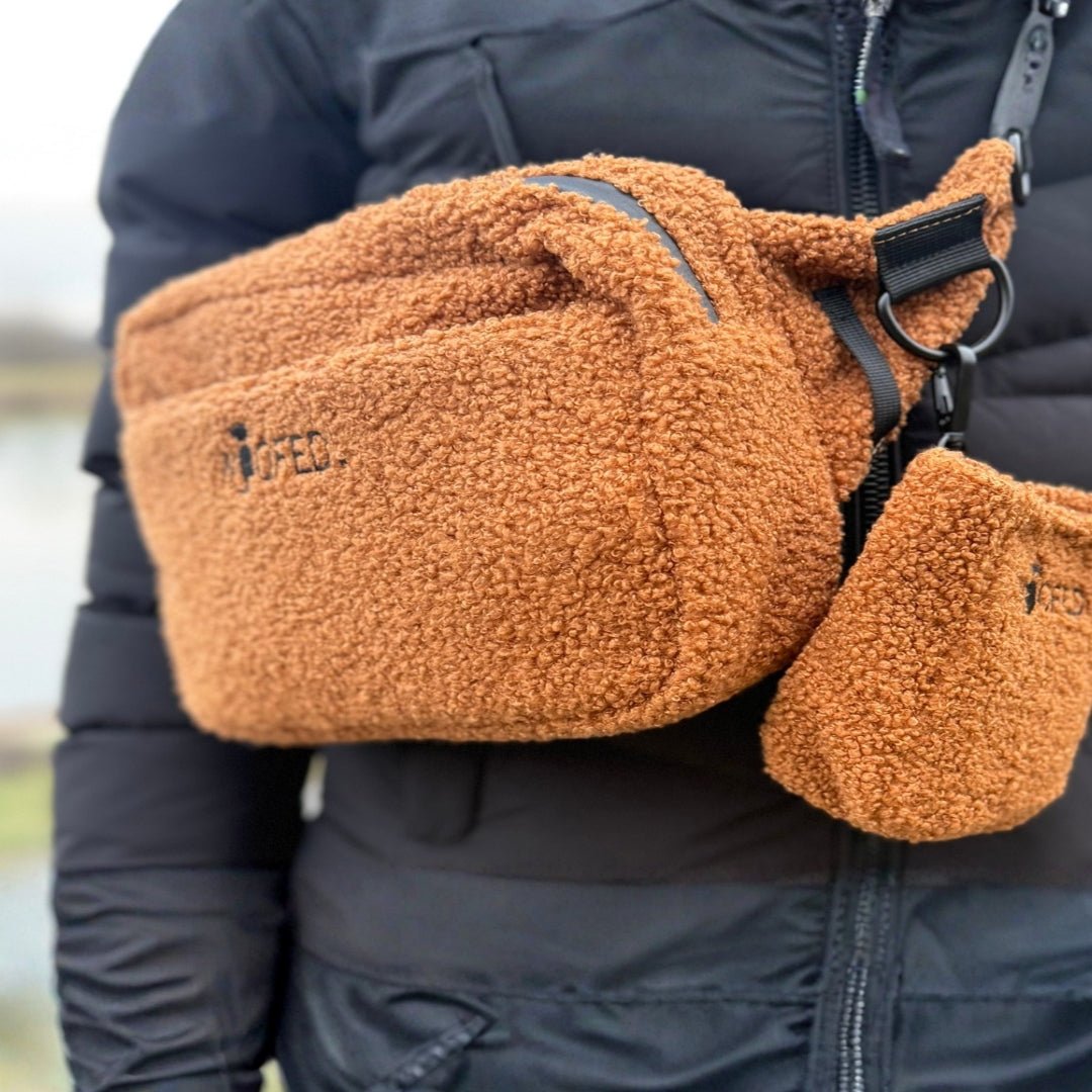 Braune Teddy-Gassitasche quer getragen auf schwarzer Jacke, flauschiges Teddy-Material, sichtbarer D-Ring und kleiner Beutel