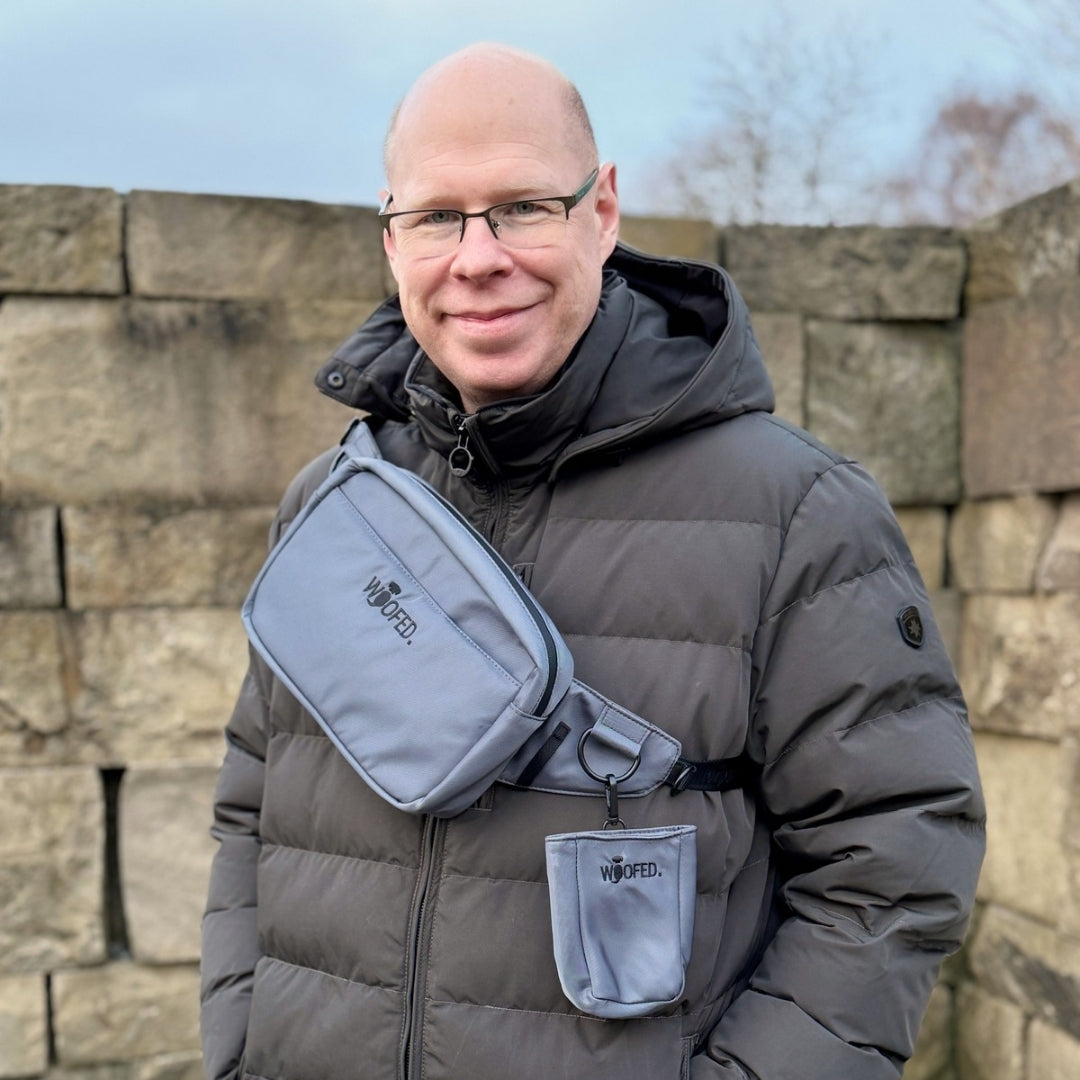 Graue Bauchtasche als Schultertasche quer über der Brust, abgerundetes Rechteck mit sichtbarem WOOFED-Logo und Leckerlibeutel