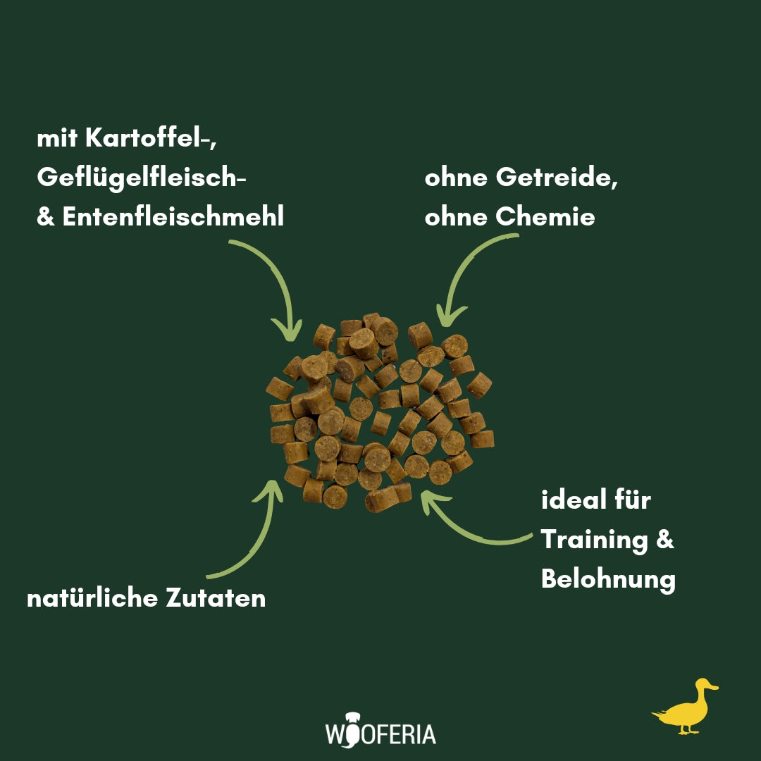 Ente Softies – braune, kleine zylindrische Leckerli im Haufen, Draufsicht auf dunkelgrünem Hintergrund mit Text