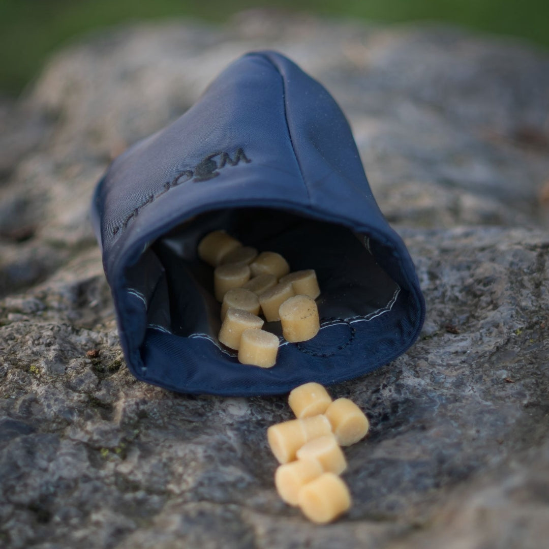 Käse Softies – beige zylinderförmige Hundeleckerlis, die aus einer dunkelblauen Tasche auf einem Felsen liegen