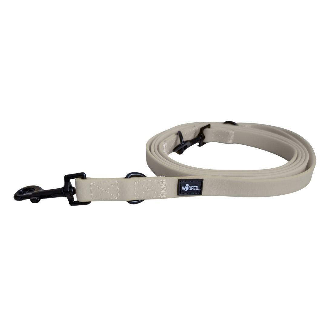 Verstellbare Führleine Desert Sand, beige gerollt mit schwarzem Karabiner, Metallringen und sichtbarem WOOFED‑Label