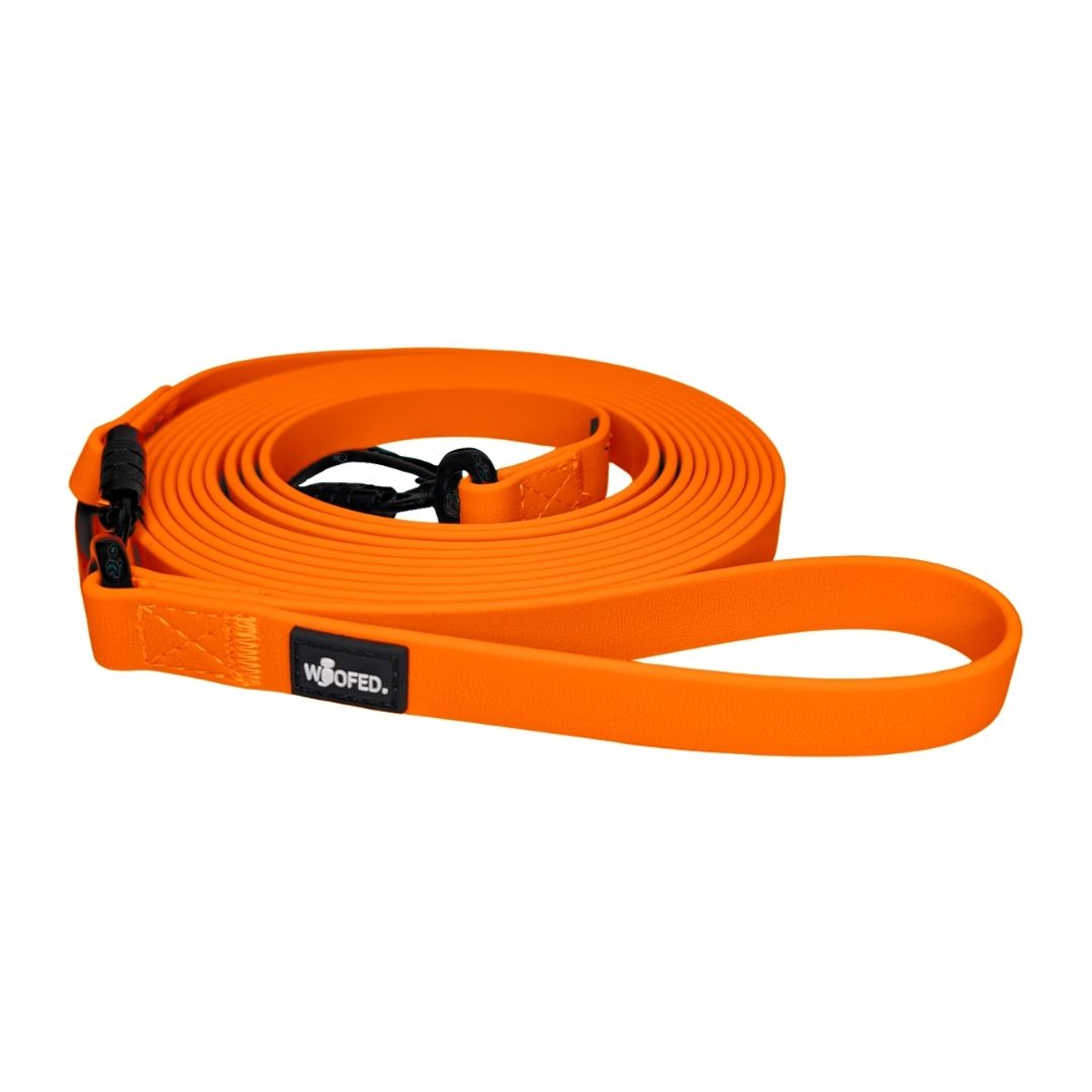 Aufgerollte, flache Schleppleine Sunset Orange mit Handschlaufe, schwarzem Karabiner und WOOFED-Logo