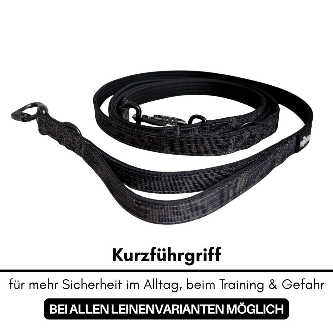 Schwarze gewebte Hundeleine mit Kurzführgriff, aufgewickelt, schwarzer Karabiner und D‑Ring sichtbar