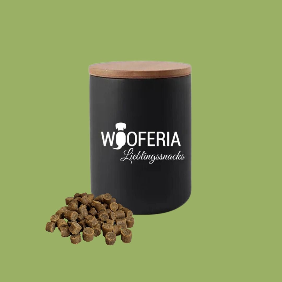 Schwarze Keramik-Leckerlidose mit Bambusdeckel, weißem WOOFERIA-Logo, Vorderansicht und brauner Snack-Haufen