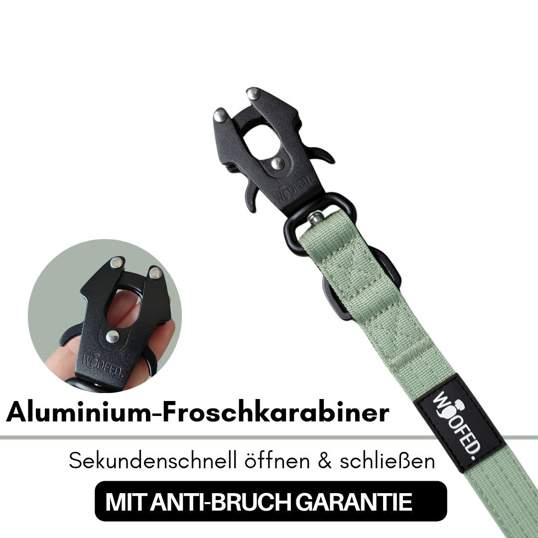 Nahaufnahme einer sagegrünen Nylon-Führleine mit schwarzem Froschkarabiner, WOOFED-Label und kleinem Einlegebild mit Hand