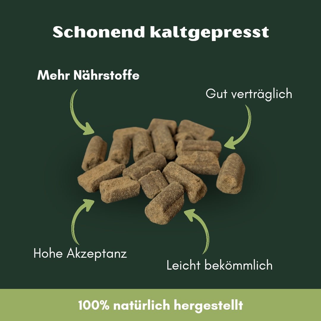 Haufen brauner, kaltgepresster Rinder-Snacks (kurze zylindrische Pellets) auf dunkelgrünem Hintergrund, Werbetext sichtbar