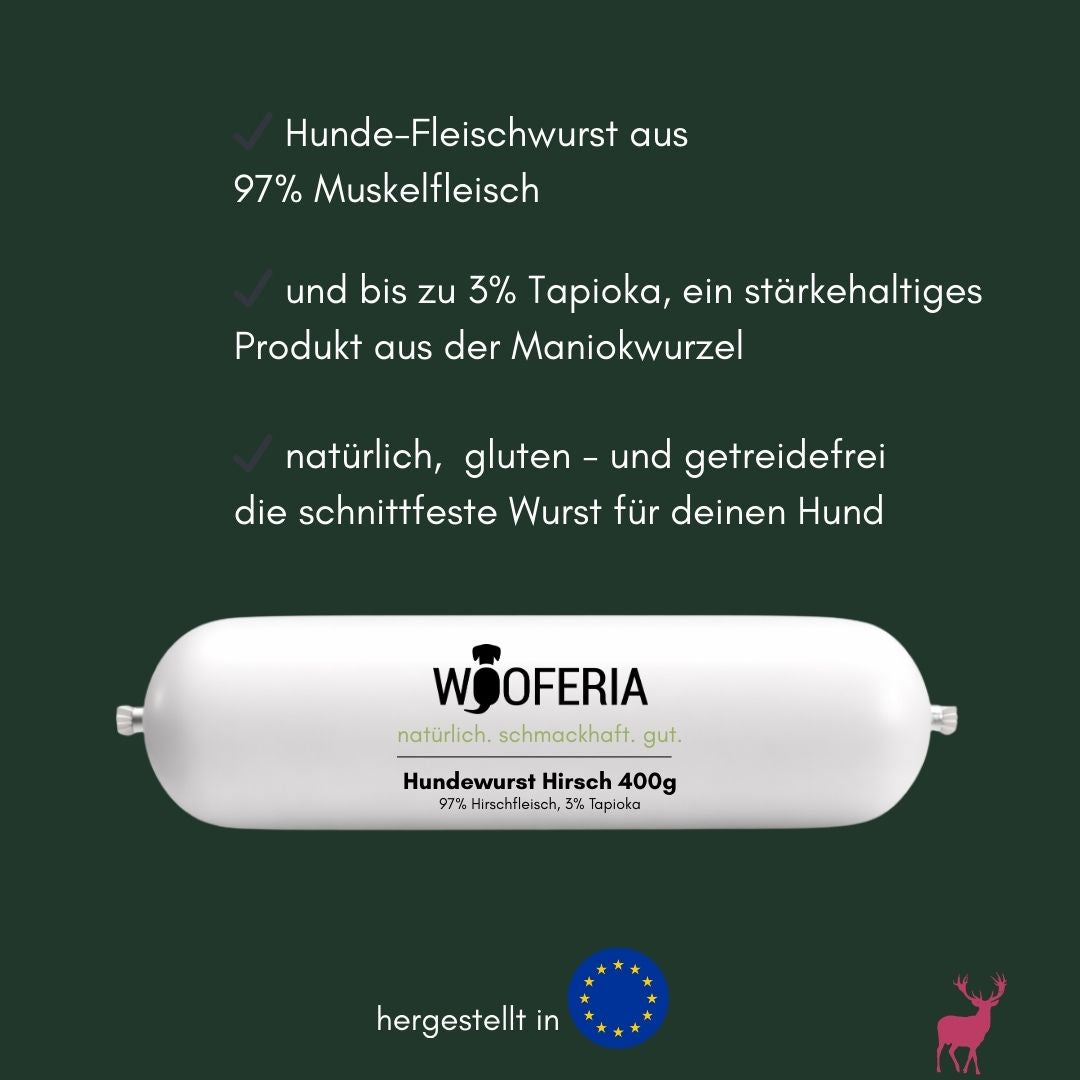 weiße, zylindrische Hundewurstrolle von Wooferia frontal gesehen, beschriftet „Hundewurst Hirsch 400g“, auf dunkelgrünem Fond