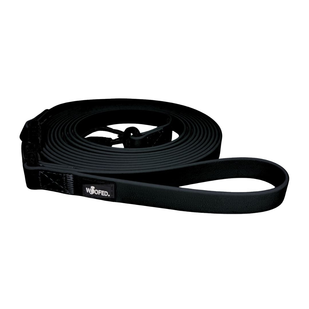 Aufgerollte schwarze Schleppleine mit flachem Band, Handschlaufe und sichtbarem Karabiner, WOOFED‑Label